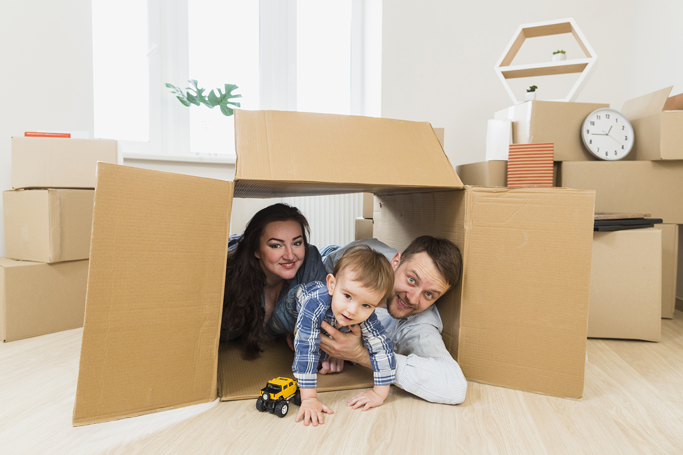 Retrato de padres felices jugando con su hijo pequeño dentro de una caja de cartón